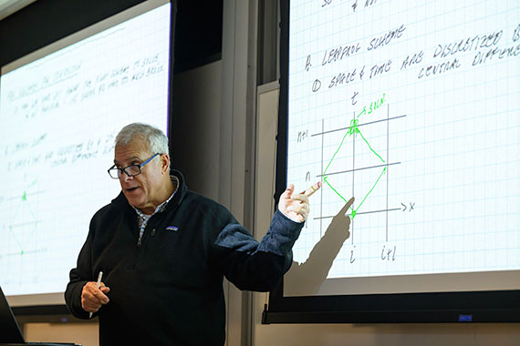 Professor David Foster points at a screen as he delivers a lecture.