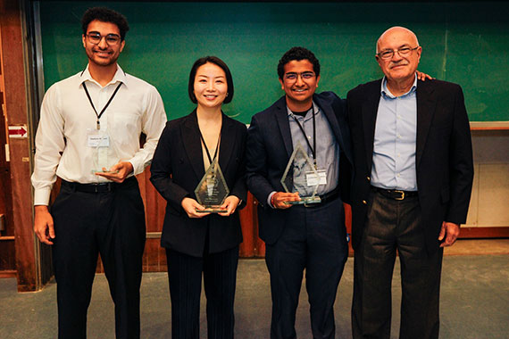 The three student winners of the Mark Ain Business Model Competition stand with Roberto Colangelo while holding their awards.