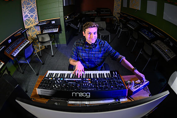 Rick Carl sits in front of Moog Muse and Moog Labyrinth synthesizers in the University of Rochester's synthesizer lab.