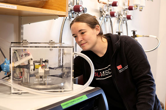 Savannah Schisler examines a clear box with mechanical equipment inside.