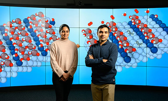 Siddharth Desphande and Snehitha Srirangam standing in front of a large screen showing molecule simulations.