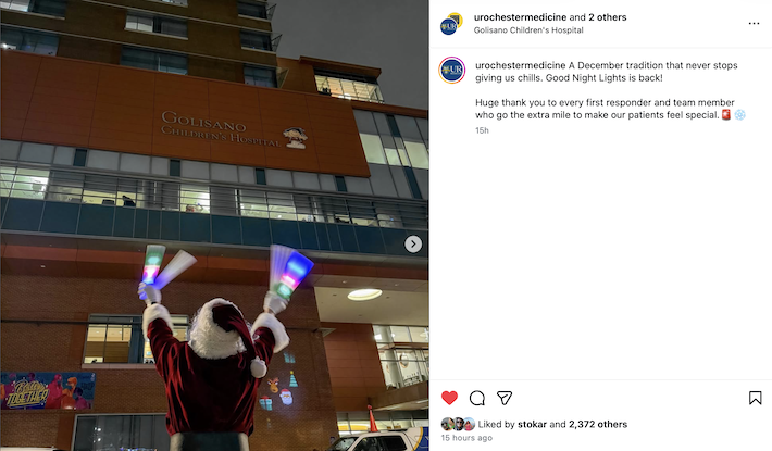 Santa, lit by law enforcement lights and vehicles, waves to children outside of Golisano Children's Hospital.