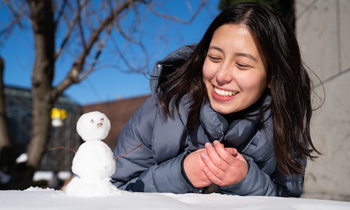 Student Chloe Yokitis builds a mini snowman on campus during the first snowfall. 