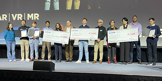 A crowd gathers onstage while three people hold giant checks.
