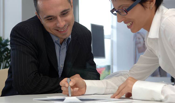 Two businesspeople smile while reviewing a piece of paper.
