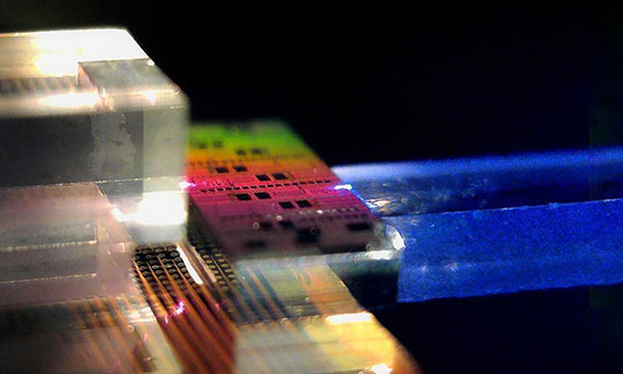 Closeup of a rainbow-hued photonic chip coupled to a clear and metallic nonlinear crystal and fiber array unit.