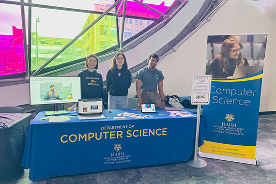 Professor Zhen Bai and two students stand at a table at the Strong National Museum of Play.