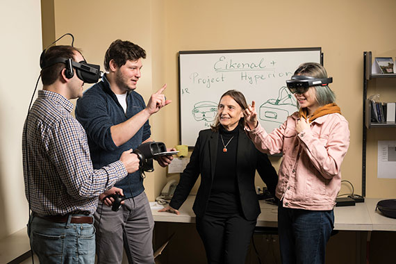Two people wearing virtual reality headsets talk with two people without headsets in a laboratory.