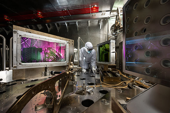 A person in protective gear works inside a high-tech laser research facility with glowing panels and precision equipment.
