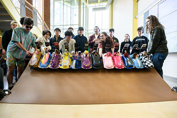 Students stand behind 12 remote-controlled cars with Barbies mounted to the top.