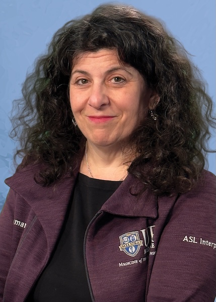 Female employee in maroon URMC jacket against a blue background. 
