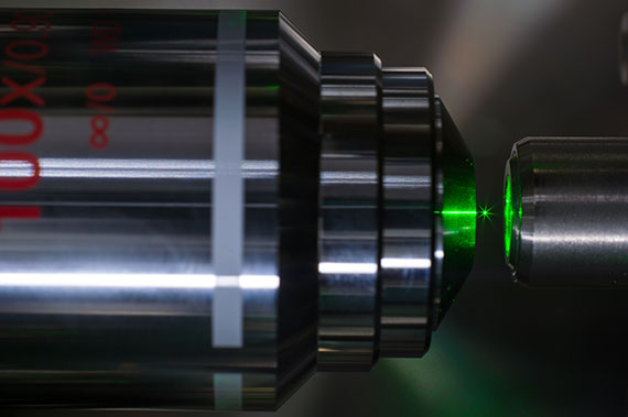 A closeup of green lasers suspending a small particle.