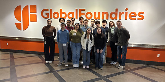 About a dozen students pose in front of a Global Foundries corporate logo.