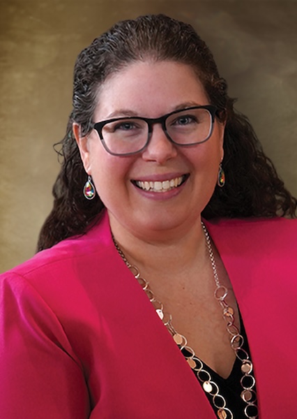 Headshot of a smiling woman in glasses wearing a pink blazer. 