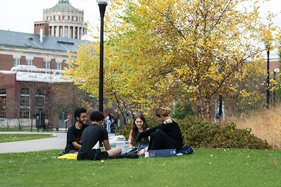 Four students sit on in a circle on the Hajim Quadrangle conducting an experiment.
