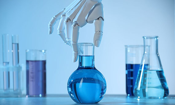 Robot hand preparing to lift a flask of blue liquid with beakers and tubes of other liquids in the background.