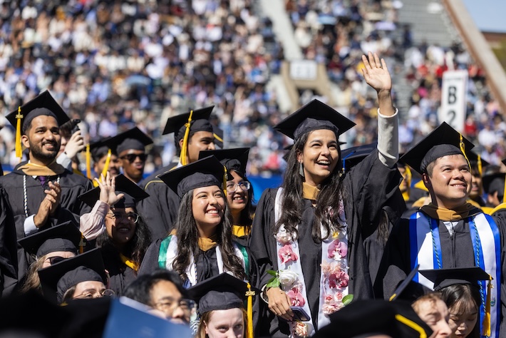 smiling graduates wave to the crowd.