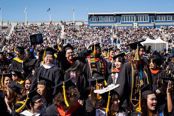 A crowd of graduates cheer during the University of Rochester Commencement ceremony at Fauver Stadium.