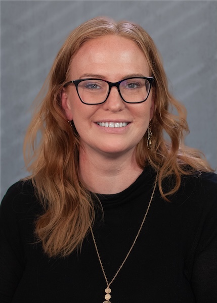 Smiling woman in black top, wearing dark-framed glasses. 