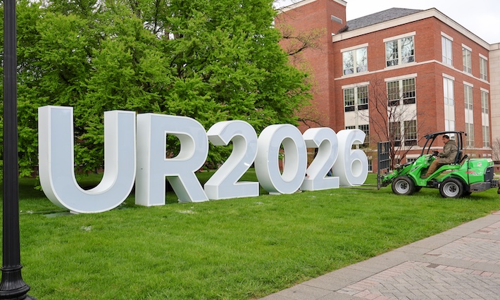 Small construction vehicle moves large UR 2026 letters onto the quad. 