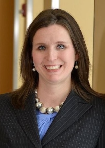 Headshot of smiling woman in black suit with blue shirt underneath. 