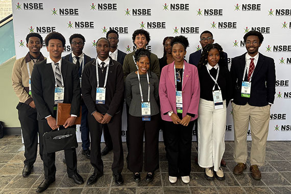Fourteen URochester students stand in front of a National Society of Black Engineers backdrop while attending a national convention.