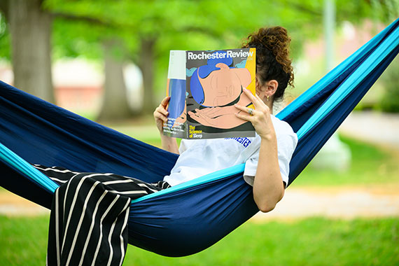 A woman in a hammock on the Eastman Quad reads the new issue of Rochester Review.