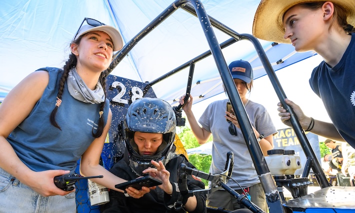 Four students in and around an off-road vehicle.