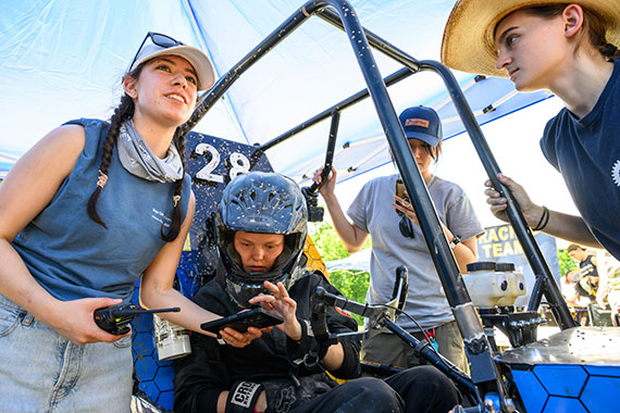 Four students huddled around an off-road vehicle discuss race results.