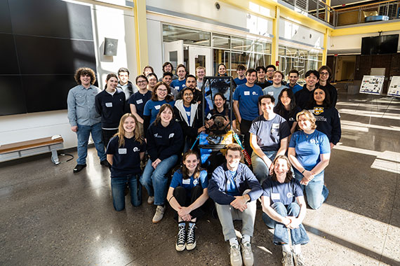 Dozens of students from the University of Rochester's Baja SAE team huddle around the car they built in Rettner Hall.