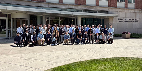 Dozens of people at attending the Center for Freeform Optics meeting gather outside Goergen Hall.
