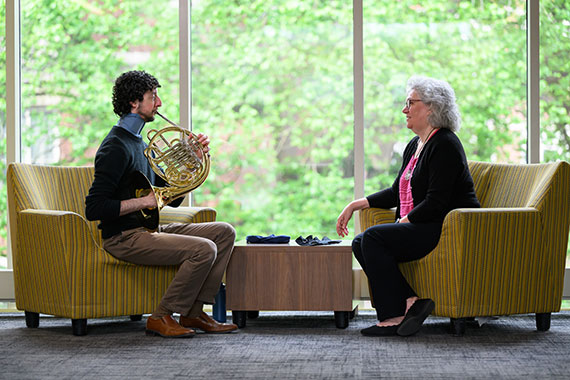 Jacob Factor plays the French horn across from Amy Lerner while wearing a neck brace designed to help with a rare throat condition.