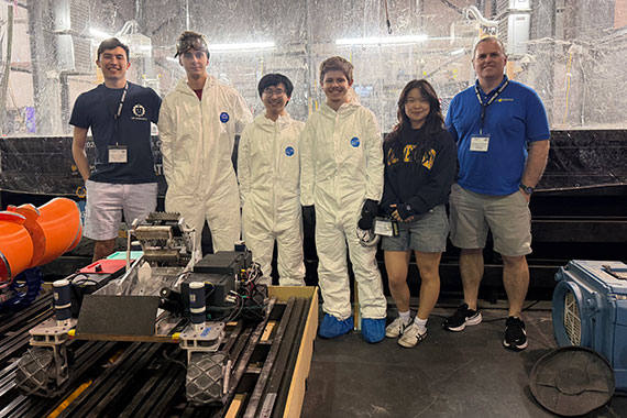 Five students and a faculty member stand in front of a robot they built for the Lunabotics competition.