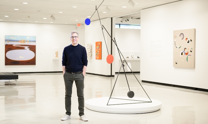 Man stands in room surrounded by modern art. 