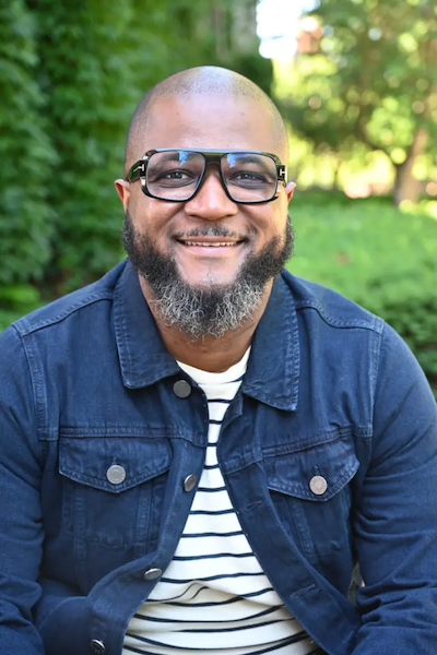 Smiling man in striped t-shirt under a navy button-down shirt. 