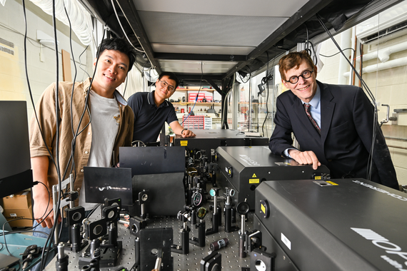Long Nguyen, Yang Xu, and Robert Boyd stand next to an optical bench with experiments.