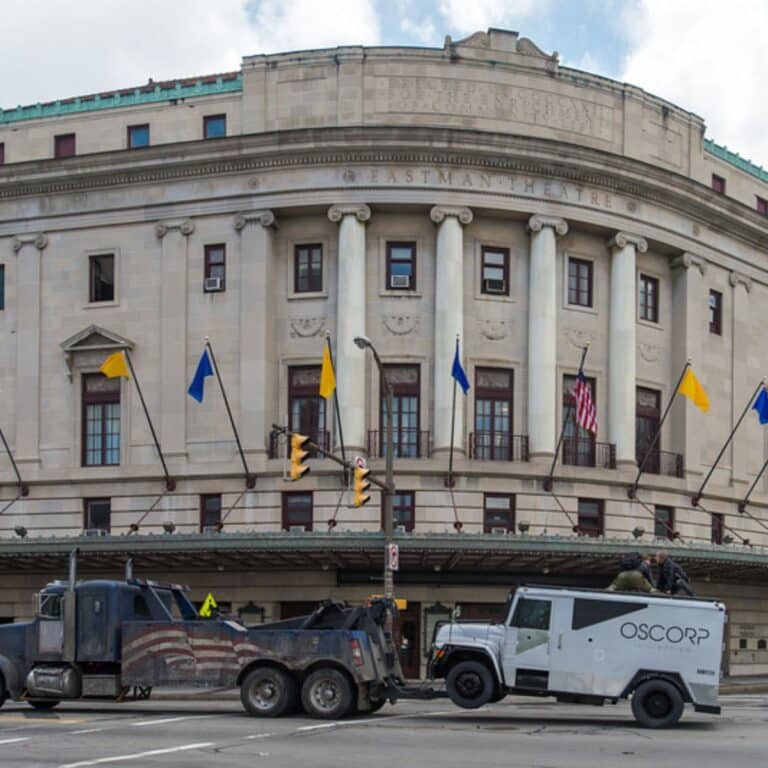 Historic theater building with columns and a towing scene involving an armored truck.