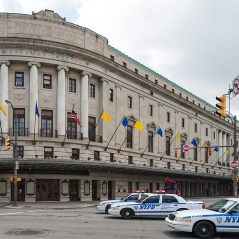 A neoclassical building with white columns and blue and yellow flags. Three NYPD police cars are parked in front.