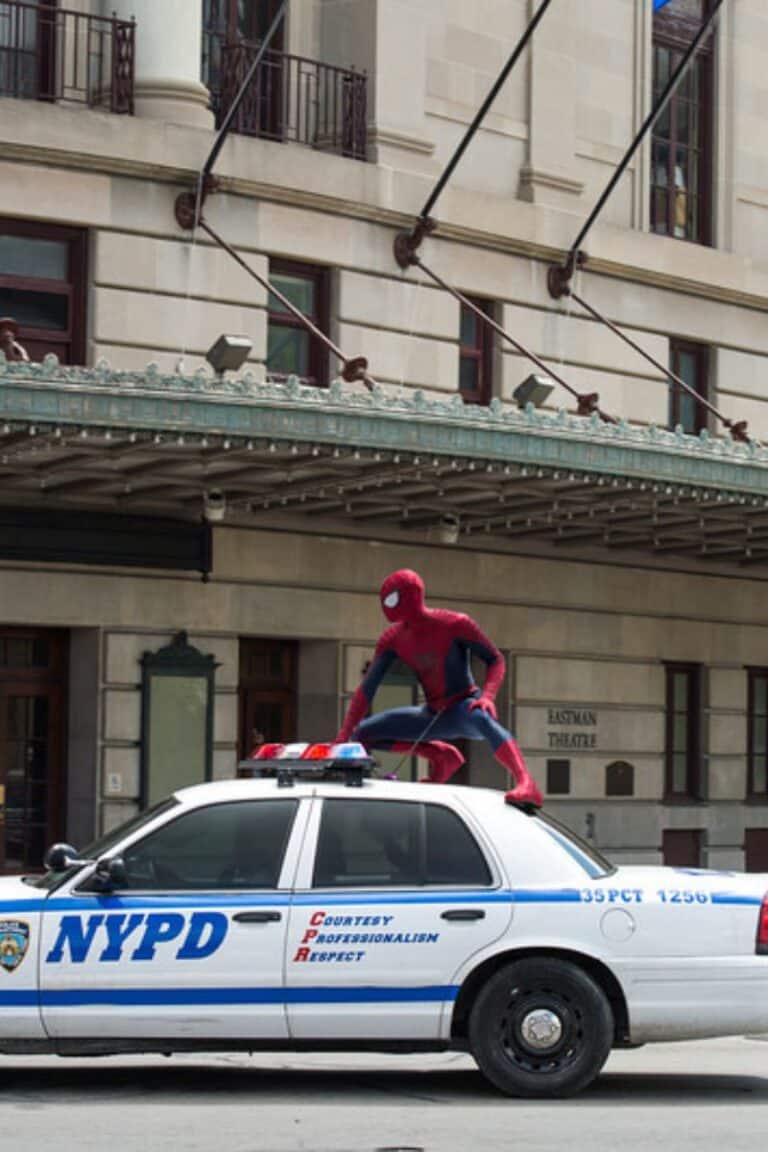 Superhero crouching on an NYPD car in front of Eastman Theatre.