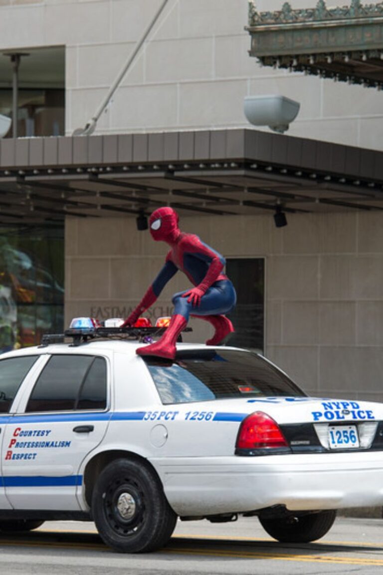 Spider-Man costume figure crouched on a white NYPD police car.