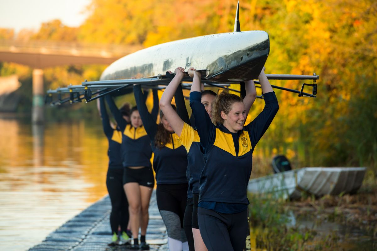 A group of rowers transporting their boat across the dock at the University of Rocheste
