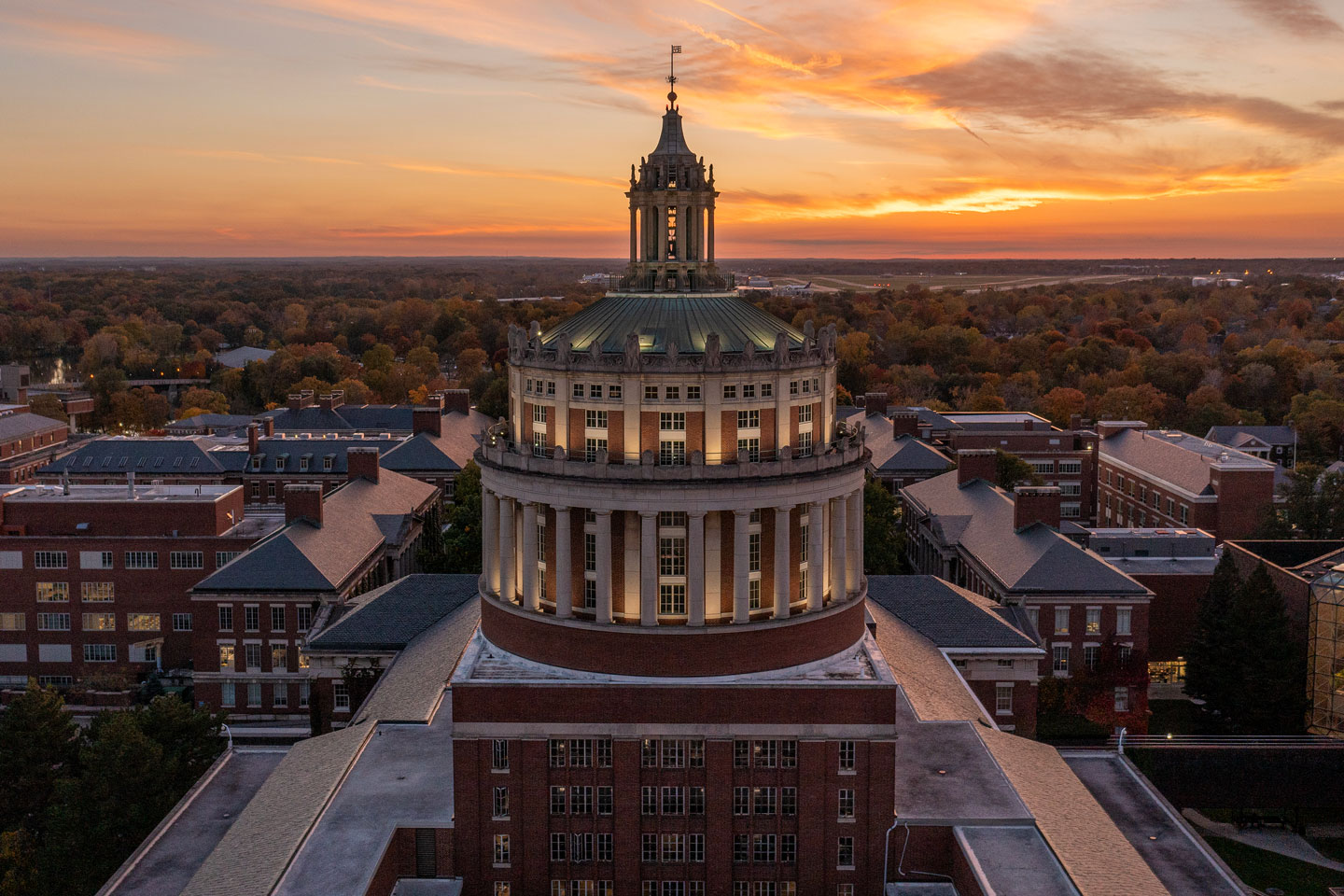 Aerial view of Rush Rhees Library at sunset, showcasing the tower against a colorful sky.