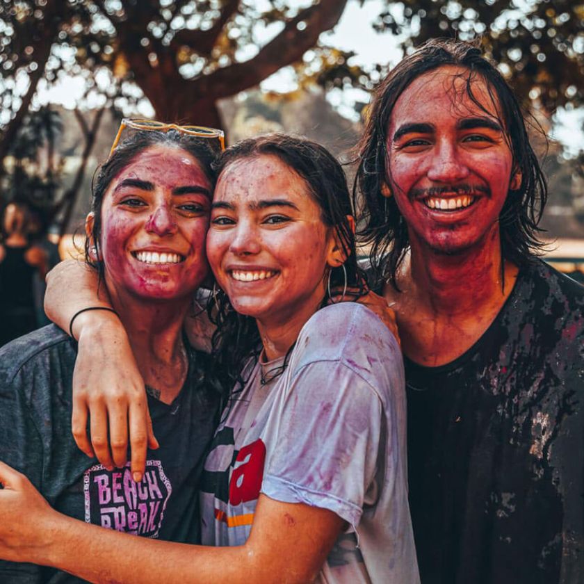 Three University of Rochester students with colorful paint on their faces, smiling and enjoying a fun moment together.