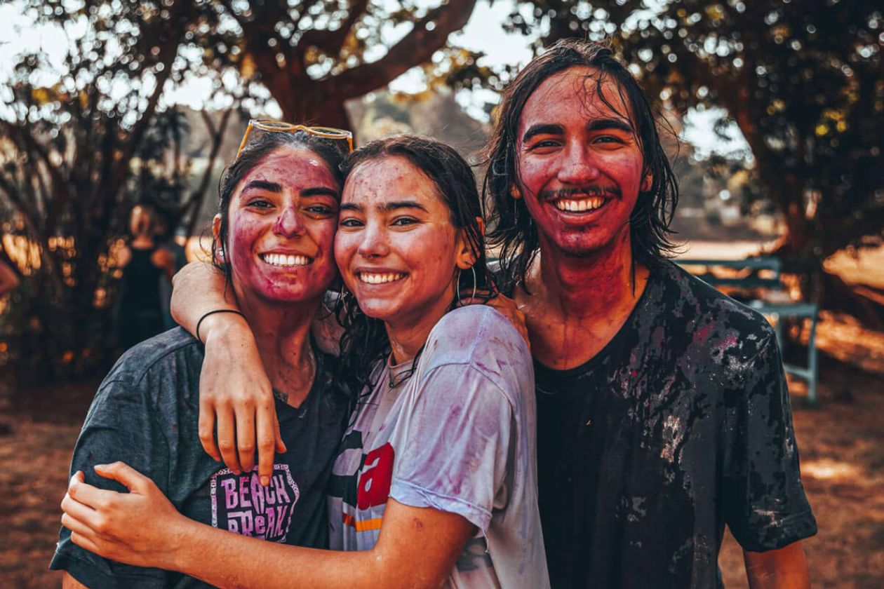 Three University of Rochester students with colorful paint on their faces, smiling and enjoying a fun moment together.