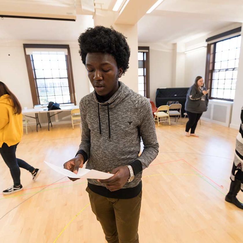 A young University of Rochester student stands in a room with several other people, engaged in conversation.