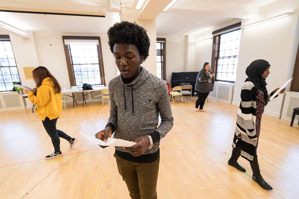 A young University of Rochester student stands in a room with several other people, engaged in conversation.