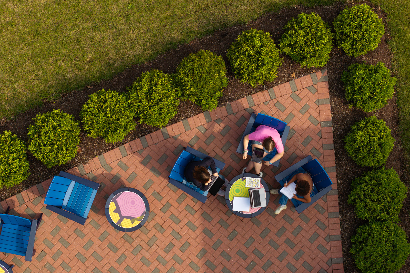 A group of people seated on chairs in a courtyard at the University of Rochester, enjoying a sunny day together.