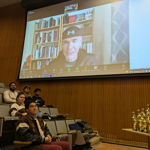 A view of an auditorium with a speaker on screen.