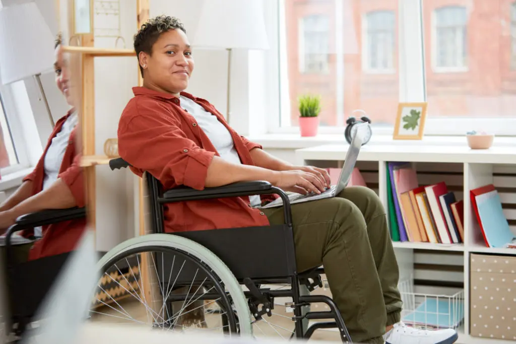 A young woman in a wheelchair working on her laptop.