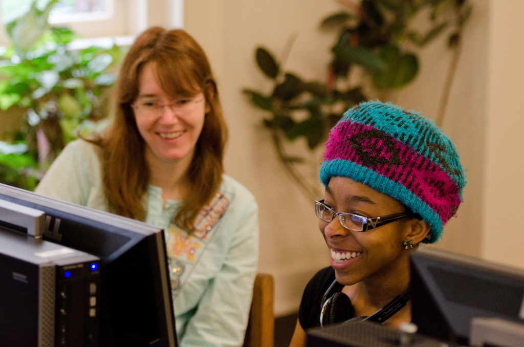 A student and a teacher looking at a computer working together